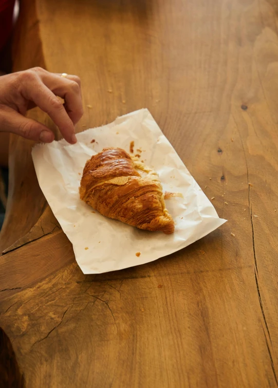 a person sitting at a table with a croissant, square, no crop, parchment, small