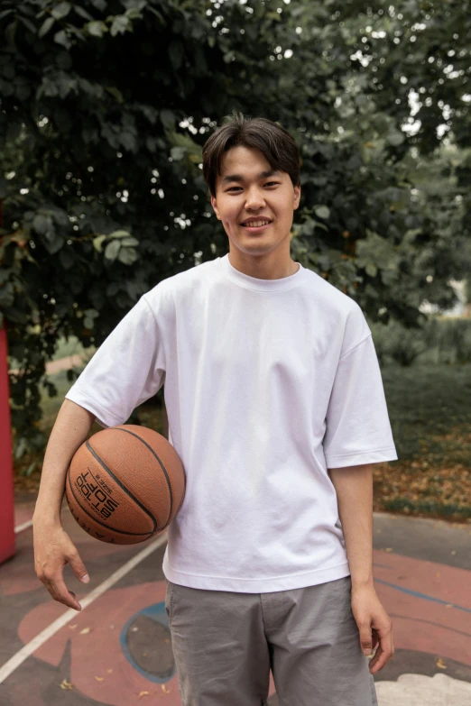 a man standing on a basketball court holding a basketball, by Jang Seung-eop, plain white tshirt, male teenager, slightly smiling, wearing a baggy