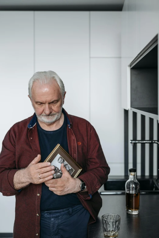 a man standing in a kitchen holding a book, by Adam Marczyński, pexels contest winner, photorealism, short white beard, portrait of an alcoholic, comforting, anthony hopkins