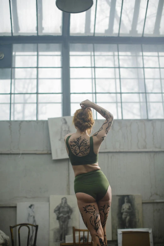 a woman standing on a stool in a room, a tattoo, inspired by Elsa Bleda, pexels contest winner, green swimsuit, in a gym, unfinished, full body cgsociety