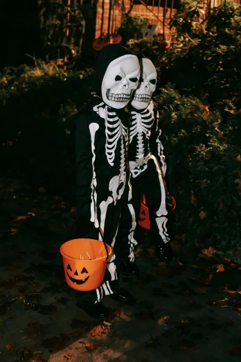 a person in a skeleton costume holding a bucket, pexels contest winner, twins, dark skinned, 2 0 1 0 s, boys