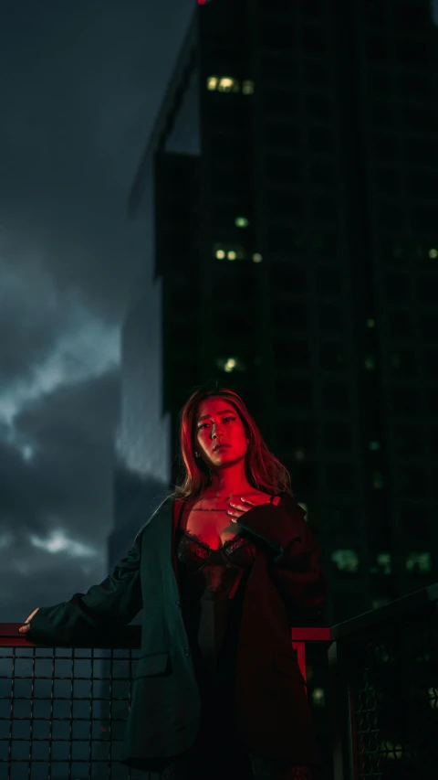 a woman sitting on a ledge in a city at night, an album cover, inspired by Elsa Bleda, pexels contest winner, realism, green and red, standing on a skyscraper rooftop, woman in black robes, woman vampire