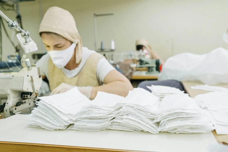 a woman working at a sewing machine in a factory, trending on unsplash, masks, piled around, azamat khairov, inspect in inventory image