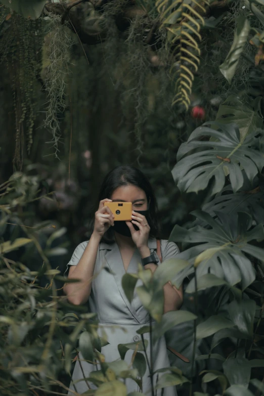 a woman taking a picture with a yellow camera, a picture, inspired by Elsa Bleda, unsplash contest winner, sumatraism, lush verdant plants, ✨🕌🌙, lush rainforest, trending on vsco