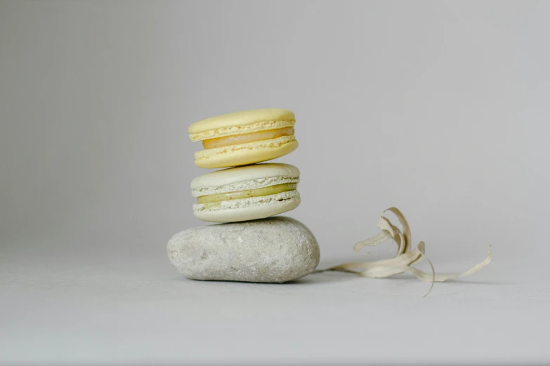 a stack of macarons sitting on top of a rock, by Emma Andijewska, minimalism, white and yellow scheme, full body photograph, silver，ivory, white clay