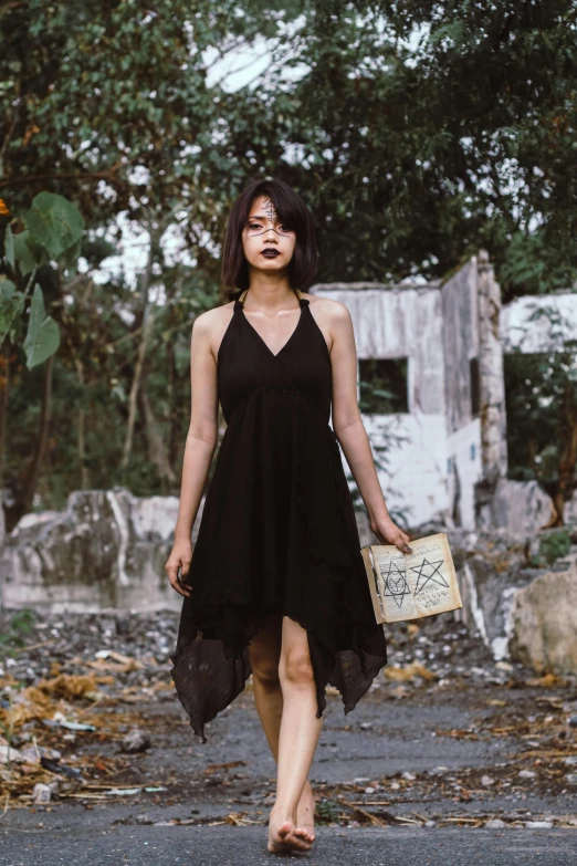 a woman in a black dress walking down a road, an album cover, pexels contest winner, bali, tattered clothing, asian woman, official store photo