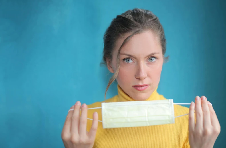 a woman holding a face mask in front of her face, pexels contest winner, yellow and blue and cyan, square, surgical supplies, mid-30s