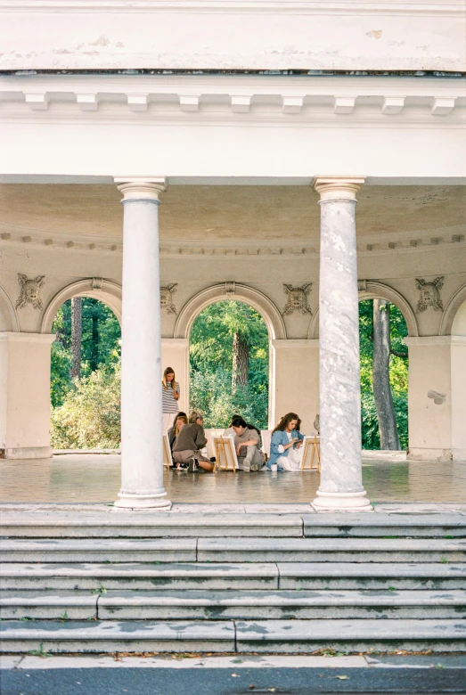 a group of people sitting on the steps of a building, an album cover, by Nina Hamnett, unsplash, art nouveau, archways made of lush greenery, picnic, white marble interior photograph, romanian