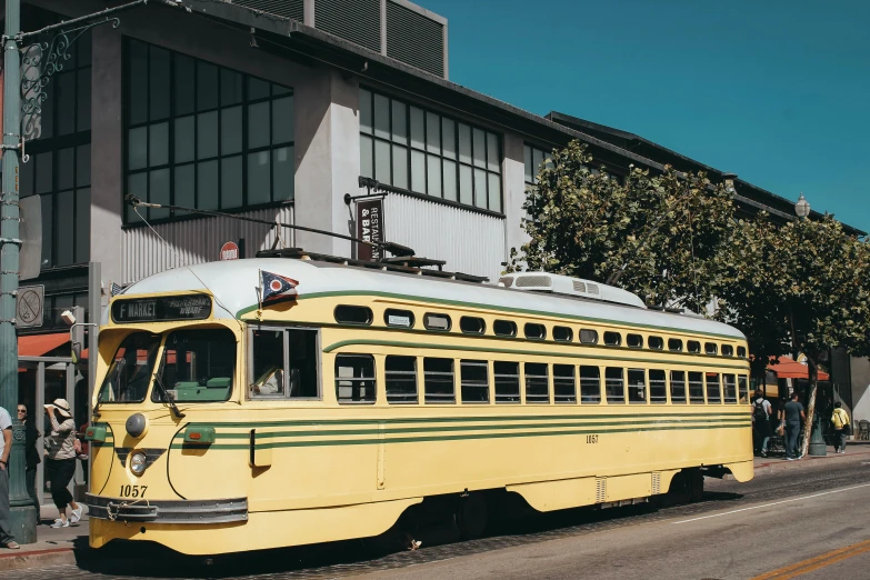 a yellow bus driving down a street next to a tall building, a colorized photo, unsplash, vallejo, 🚿🗝📝, an olive skinned, street tram