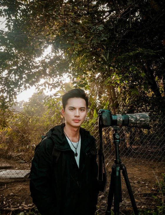 a man standing next to a camera on a tripod, by Robbie Trevino, against the backdrop of trees, ruan cute vtuber, ((portrait)), postprocessed)