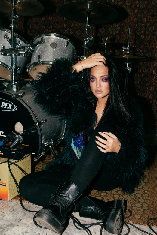 a woman sitting on the floor next to a drum, an album cover, inspired by Elsa Bleda, trending on pexels, renaissance, long raven hair, portrait of vanessa morgan, menacing pose, synthetic fur