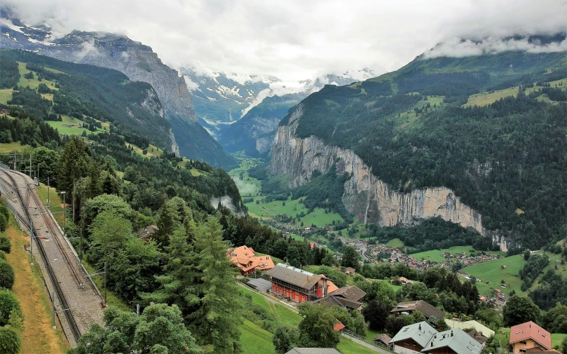 a train traveling through a lush green valley, inspired by Peter Zumthor, pexels contest winner, hurufiyya, lauterbrunnen valley, buildings carved out of stone, panoramic view, college