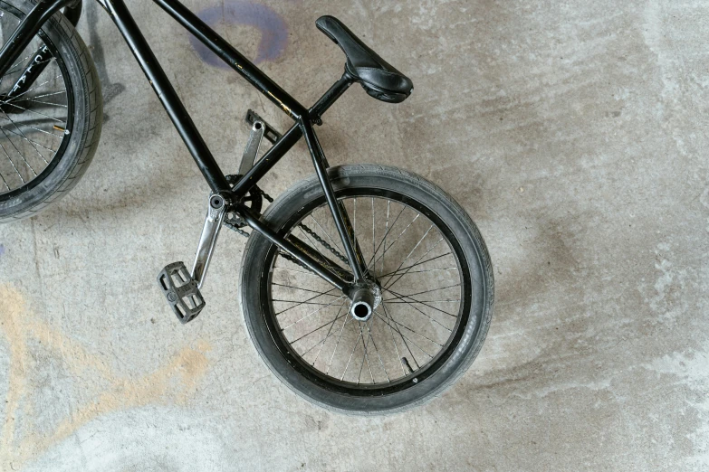 a black bicycle sitting on top of a cement floor, at a skate park, top - down photograph, detailed product image, complaints