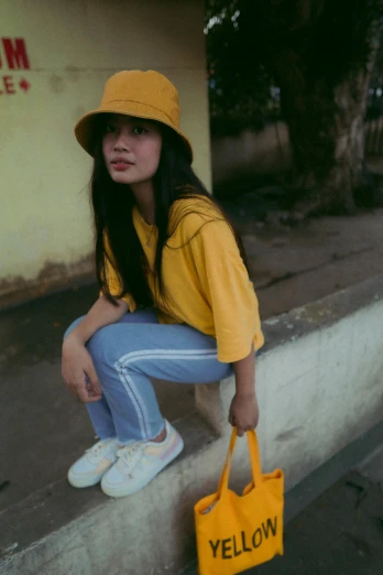 a woman sitting on a curb with a yellow bag, a picture, by Yosa Buson, trending on pexels, bucket hat, ulzzang, gif, low lighting