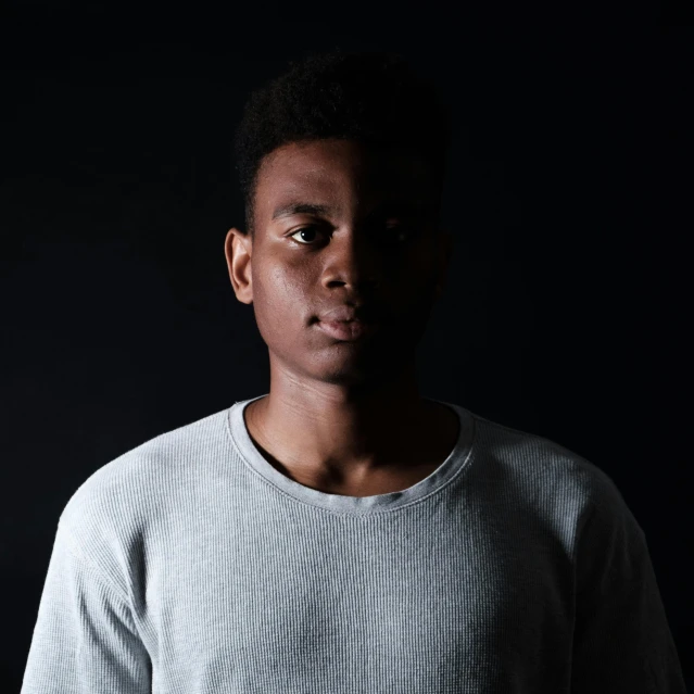 a man standing in front of a black background, by Nadir Afonso, teenage boy, light skin, on a gray background, looking serious