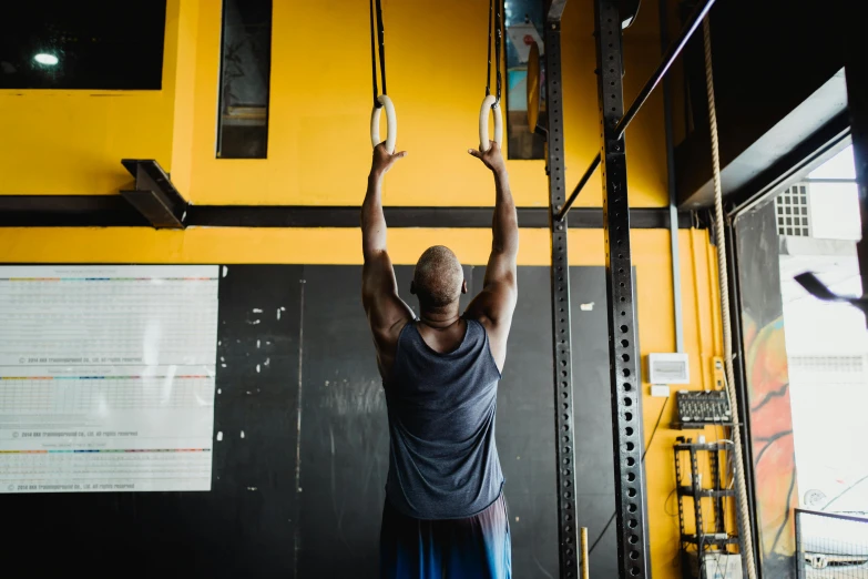 a man doing pull ups in a gym, a photo, by Lee Loughridge, pexels contest winner, hurufiyya, yellow and charcoal, tall thin build, background image, lachlan bailey