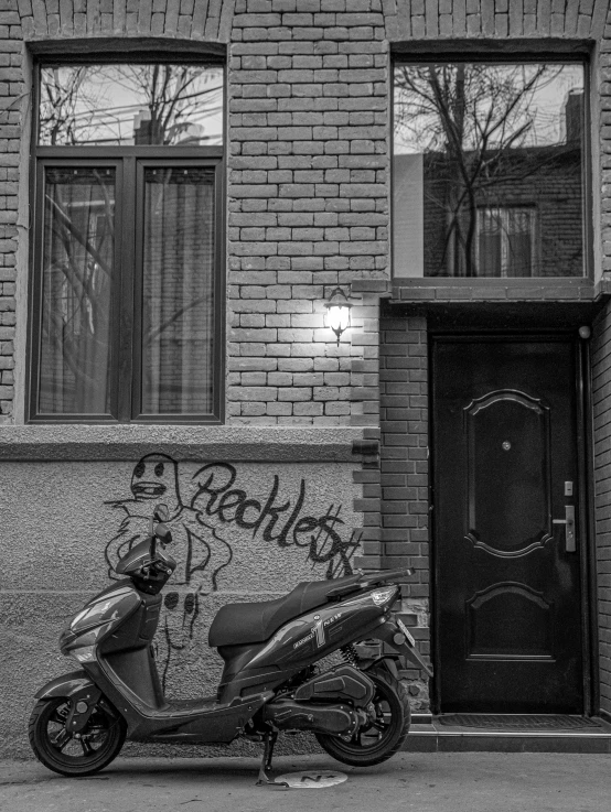 a scooter parked in front of a brick building, by andrei riabovitchev, black and white image, set photo, grafitti, rachel wall