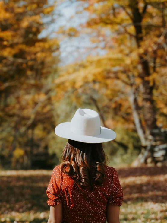 a woman in a red dress and a white hat, by Maggie Hamilton, pexels contest winner, fall foliage, back of head, 🐎🍑, white and orange