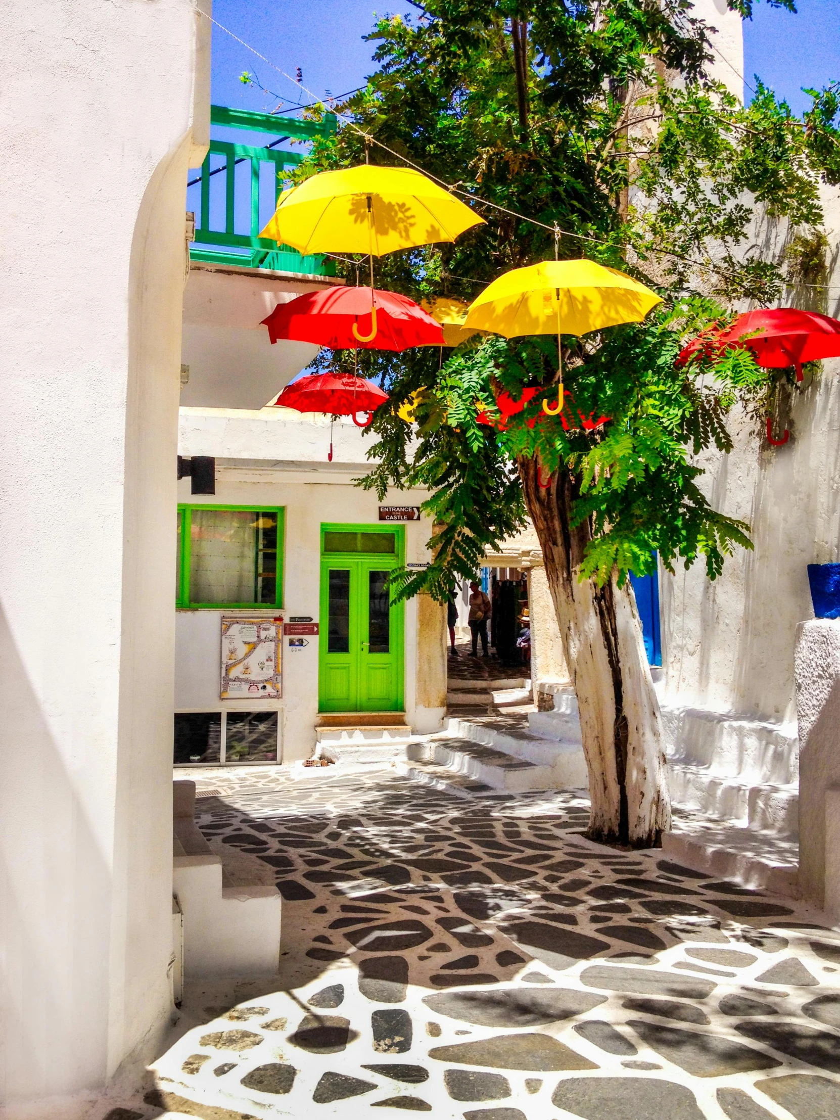 a group of umbrellas hanging from the side of a building, pathos, whitewashed buildings, full of colour, green alleys