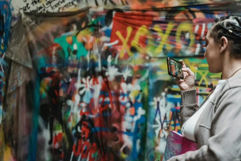 a woman standing in front of a wall covered in graffiti, a picture, by Micha Klein, pexels contest winner, graffiti, pewdiepie selfie at a bridge, hold up smartphone, grungy; colorful, blurred photo