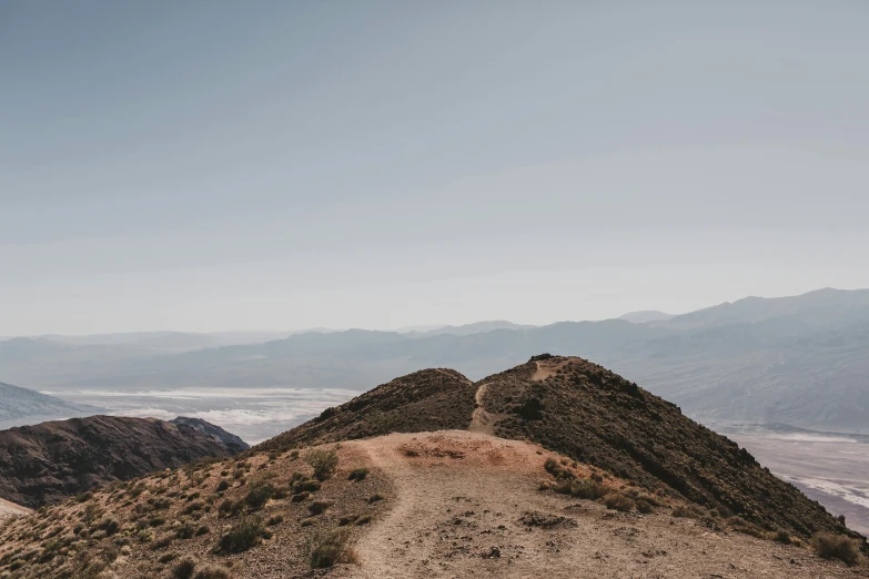 a person standing on top of a mountain, by Ryan Pancoast, unsplash contest winner, death valley, rocky ground with a dirt path, clear skies in the distance, be running up that hill