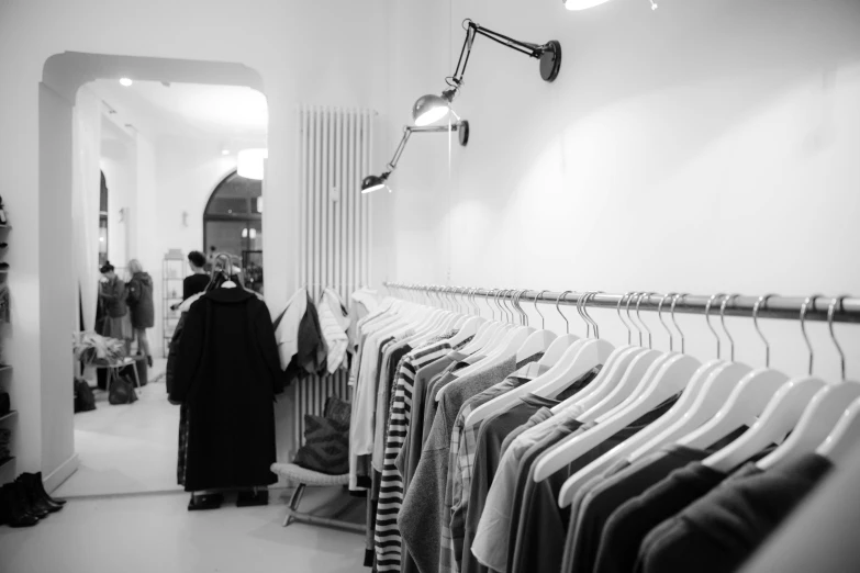 a person standing in front of a rack of clothes, a black and white photo, by Matthias Weischer, unsplash, dezeen showroom, customers, light greyscale, mezzanine