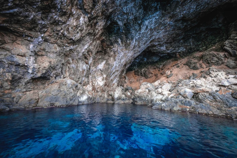 a cave in the middle of a body of water, dark blue water, swimming