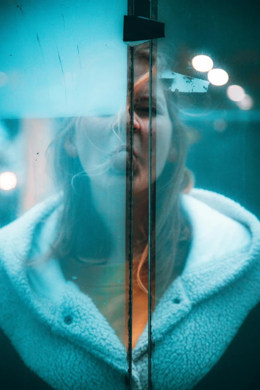 a woman standing in front of a glass door, inspired by Elsa Bleda, pexels contest winner, visual art, wearing a neon blue hoodie, mirroring, half face, movie photo