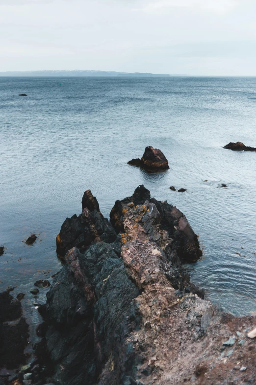 a man standing on top of a rock next to the ocean, jagged rocks, distant photo, pembrokeshire, nature photo