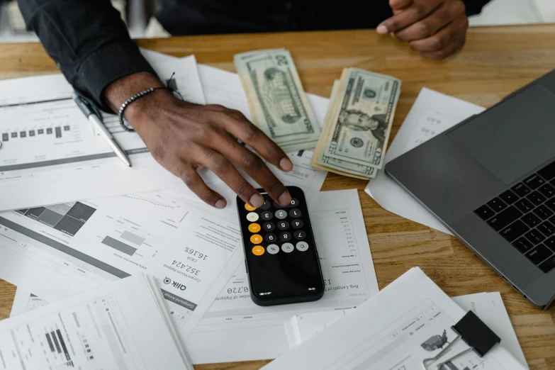 a man that is sitting at a table with a calculator, by Carey Morris, pexels contest winner, hurufiyya, piles of money, man is with black skin, high quality screenshot, holding scale