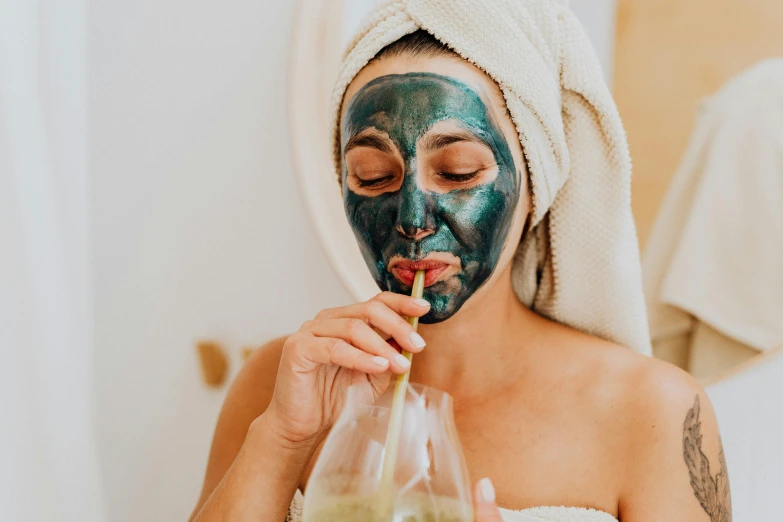 a woman is putting a mask on her face, trending on pexels, bubbly, wearing only a green robe, charcoal and champagne, manuka