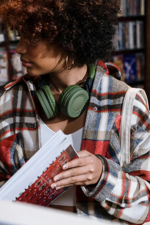 a woman reading a book while wearing headphones, an album cover, trending on pexels, happening, green and brown clothes, wearing plaid shirt, bookshops, wearing a turtleneck and jacket