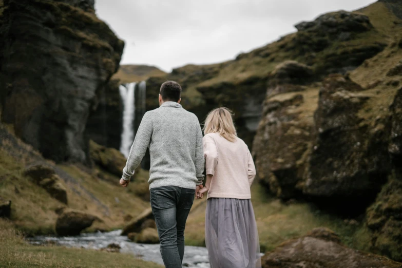 a man and woman walking in front of a waterfall, by Hallsteinn Sigurðsson, pexels contest winner, hurufiyya, holding hands, background image, thumbnail, casually dressed