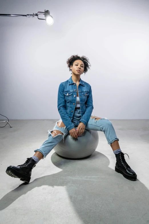 a woman sitting on top of a ball in a room, an album cover, trending on pexels, graffiti, wearing a jeans jackets, light skin, non binary model, confident pose