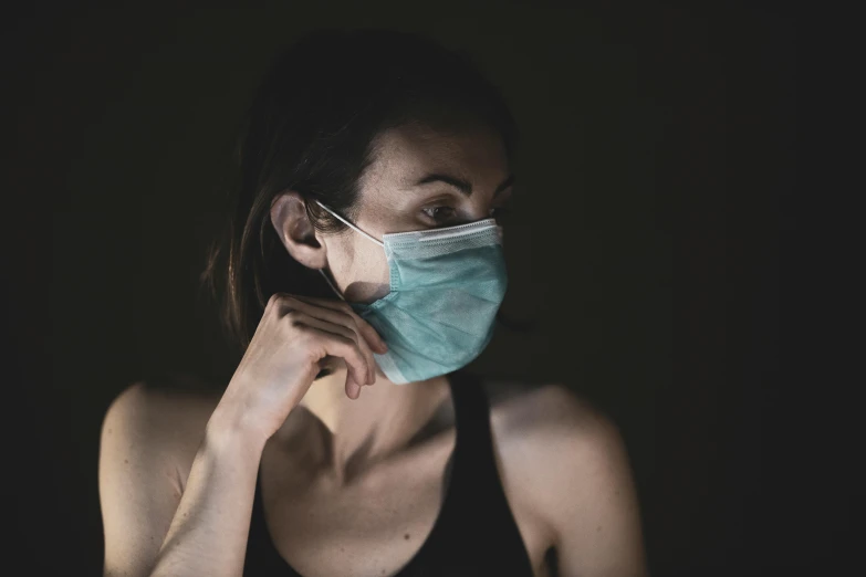 a woman wearing a face mask in the dark, a photo, pexels, healthcare worker, hand on her chin, profile pic, face covers half of the frame