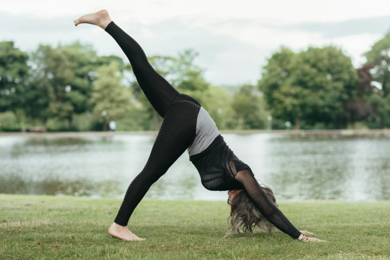 a woman doing a handstand in a park, by Rachel Reckitt, leggings, black, kami, grey