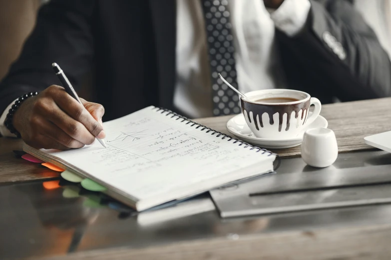 a man sitting at a desk writing in a notebook, a drawing, trending on unsplash, wearing a pinstripe suit, next to a cup, 9 9 designs, te pae