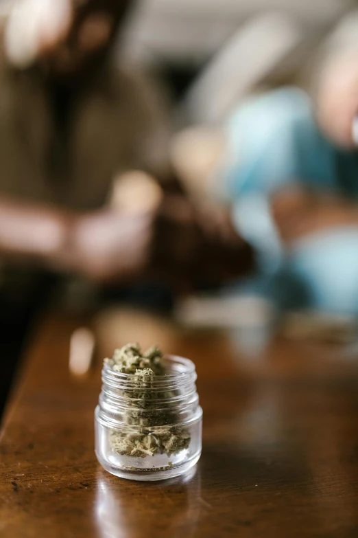 a jar of marijuana sitting on top of a wooden table, a portrait, trending on pexels, group sit at table, thumbnail, 1 2 9 7, compassionate