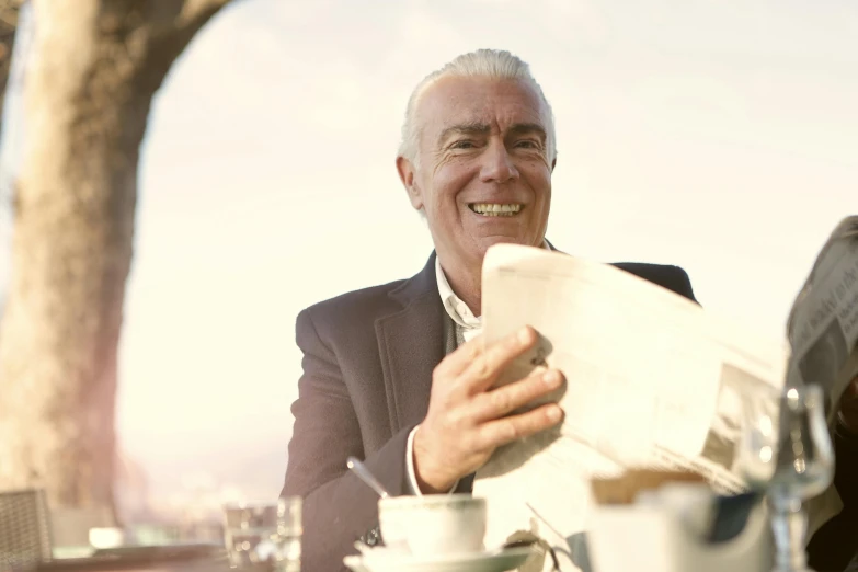 a man sitting at a table with a newspaper in his hand, a photo, by Gavin Nolan, pexels contest winner, white haired, with an elegant smile, 15081959 21121991 01012000 4k, sunny sky