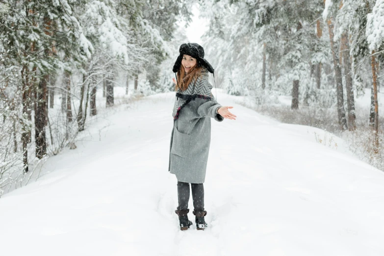 a woman standing in the middle of a snowy road, inspired by Louisa Matthíasdóttir, pexels contest winner, doing a sassy pose, grey, wearing festive clothing, straw hat and overcoat