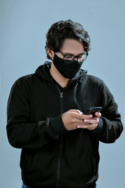 a man wearing a face mask looking at his cell phone, pexels, wearing a black sweater, on a gray background, ismail, finely masked