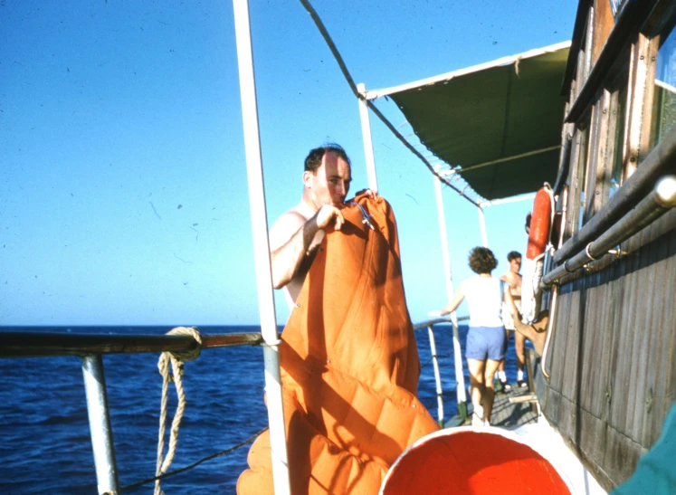 a group of people standing on top of a boat, gutai group, diving suit, orange, carrying big sack, 1960s color photograph