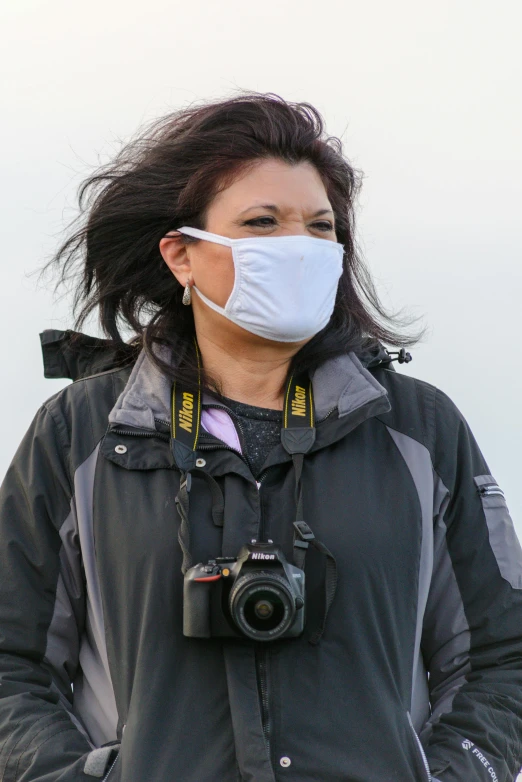 a woman wearing a face mask and holding a camera, grey mist, wearing a flying jacket, coronavirus, 2022 photograph