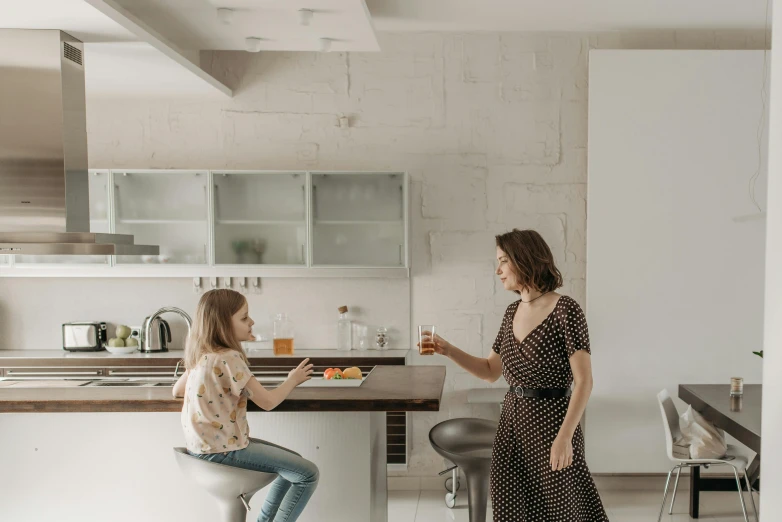 a woman standing next to a woman in a kitchen, by Will Ellis, pexels contest winner, altermodern, sitting on a mocha-colored table, family friendly, but minimalist, panoramic view of girl