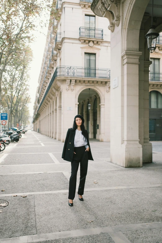 a woman standing on a sidewalk in front of a building, black suit pants, parisian buildings, mei-ling zhou, in town