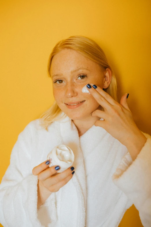 a woman in a bathrobe brushing her teeth, by Julia Pishtar, reddit, happening, dark circles under bemused eyes, blonde cream, in front of an orange background, synthetic bio skin