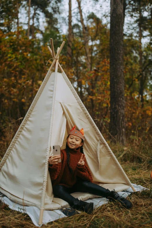 a woman sitting in a teepee in the woods, a portrait, by Natasha Tan, pexels contest winner, young asian girl, looking at his phone, autum, children's