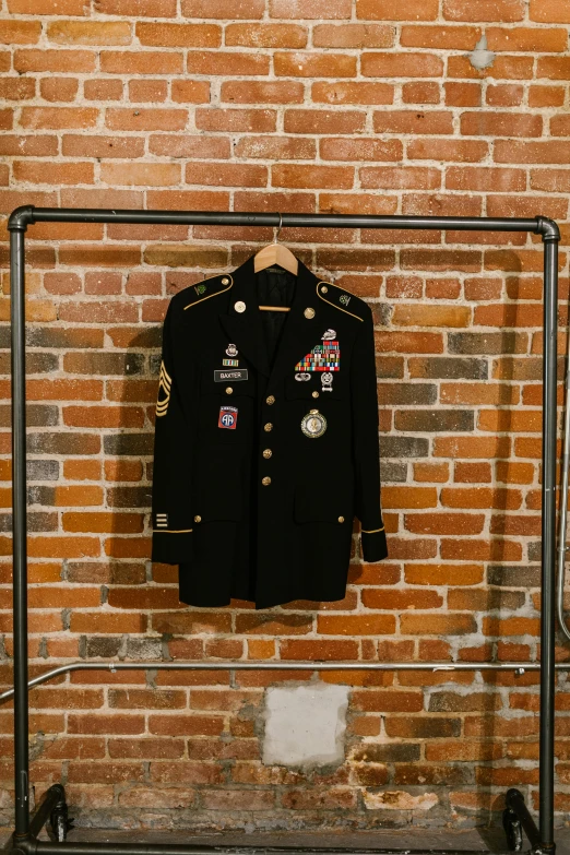 a jacket hanging on a rack in front of a brick wall, in black military uniform, honored, on display, center frame medium shot