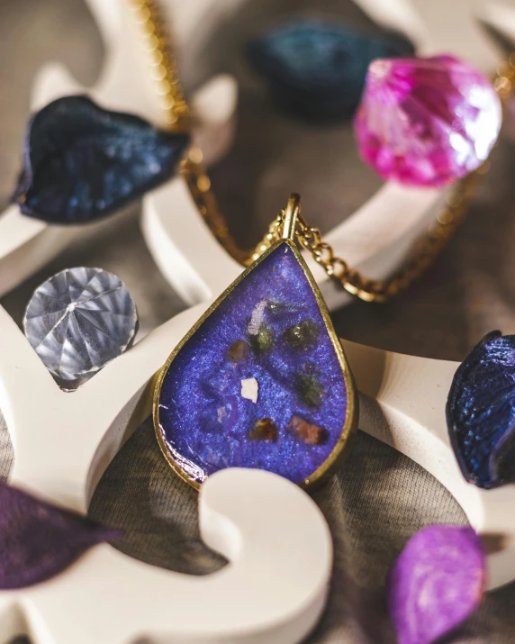 a close up of a necklace on a table, by Julia Pishtar, purple sand, blue and gold palette, galaxy in a bottle, product display photograph