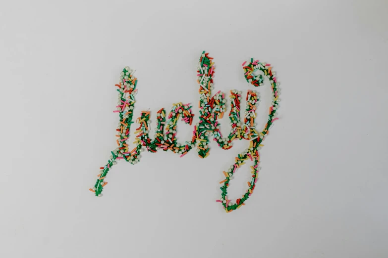 the word joy spelled out of sprinkles on a white surface, an album cover, by Lucette Barker, trending on pexels, graffiti, lucky star, embroidered velvet, circuit, clover